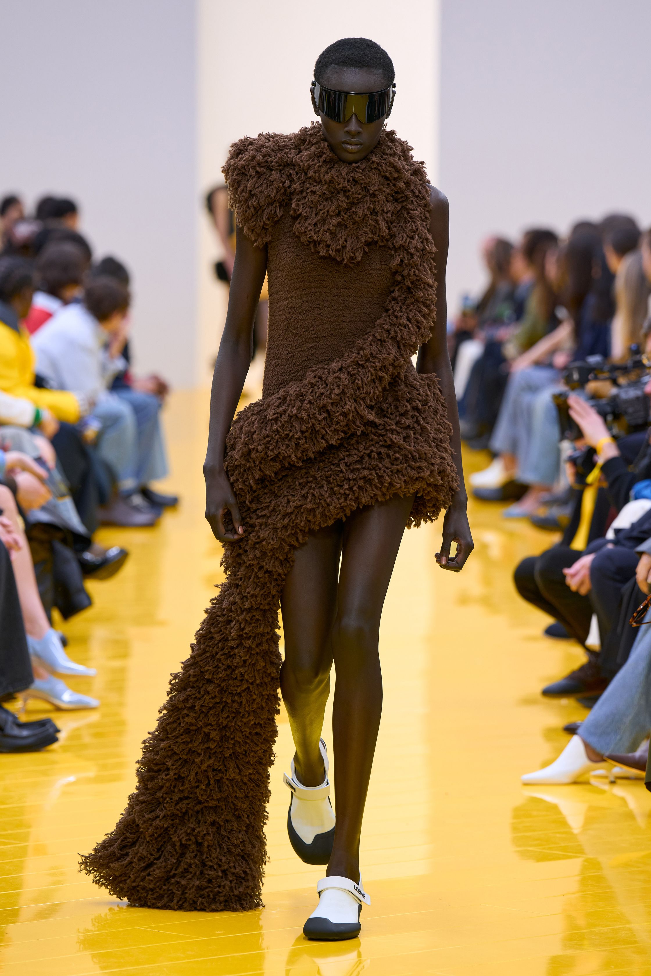 Jonathan Anderson 为 Loewe 带来一场充满艺术实验的秀：黄色地面与鲜明色彩形成强烈视觉舞台，极简廓形针织、雕塑化皮革外套、夸张毛绒结构和实验比例裙装共同构建一种“可穿戴雕塑”。从鲜黄、亮蓝到浓郁棕色毛绒，材质对比成为本季核心语言，既有幽默感也带有博物馆式艺术气质-顽石频道趋势研究